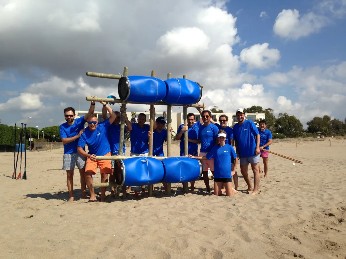 Un grupo sostiene una estructura con barriles azules en la playa.
