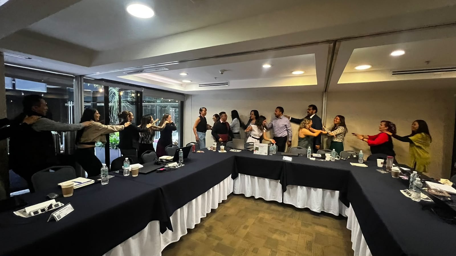 Participants collaborate in a standing activity around meeting tables.