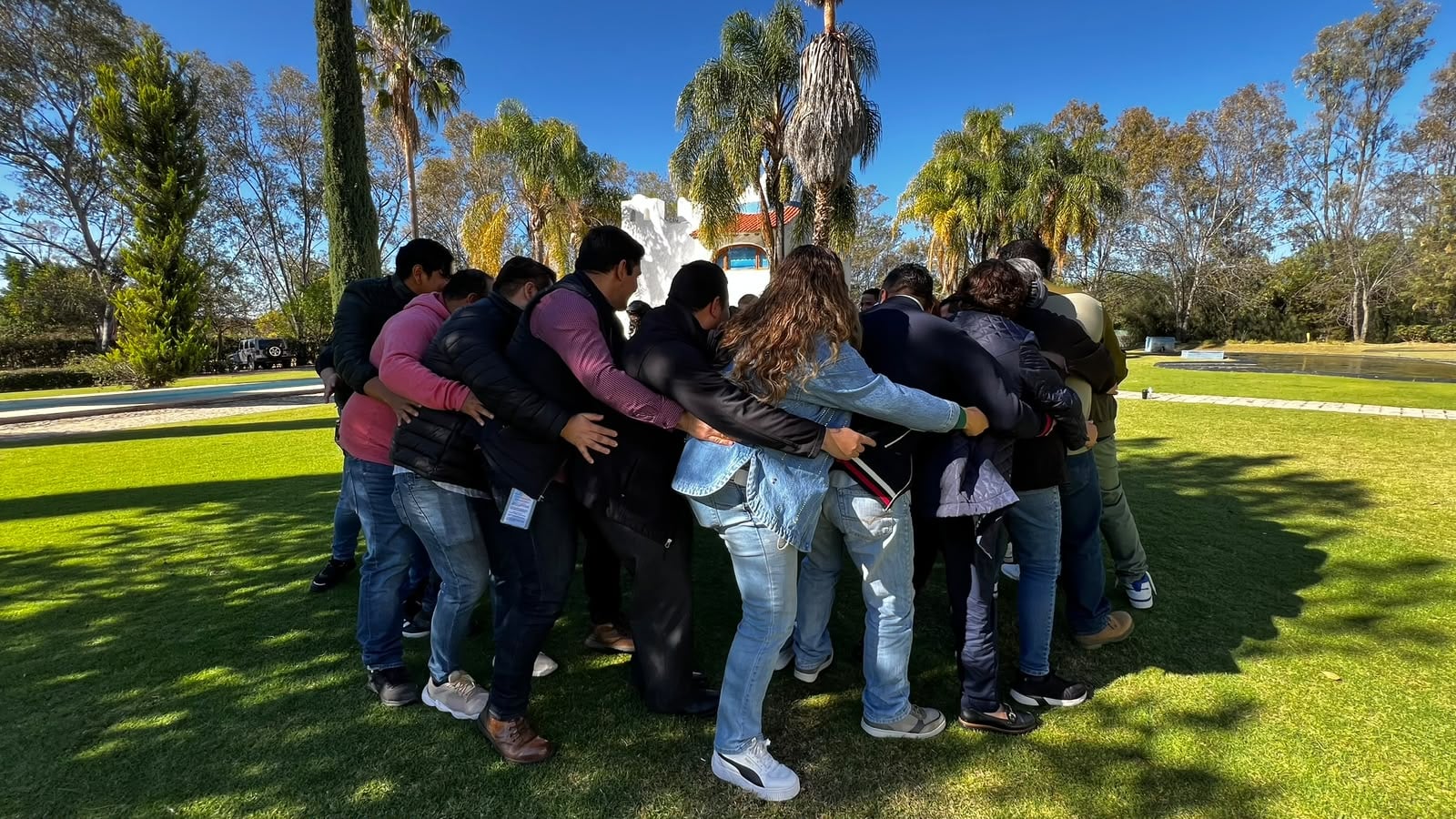 Participants stand in a close circle with arms around each other during an outdoor activity.